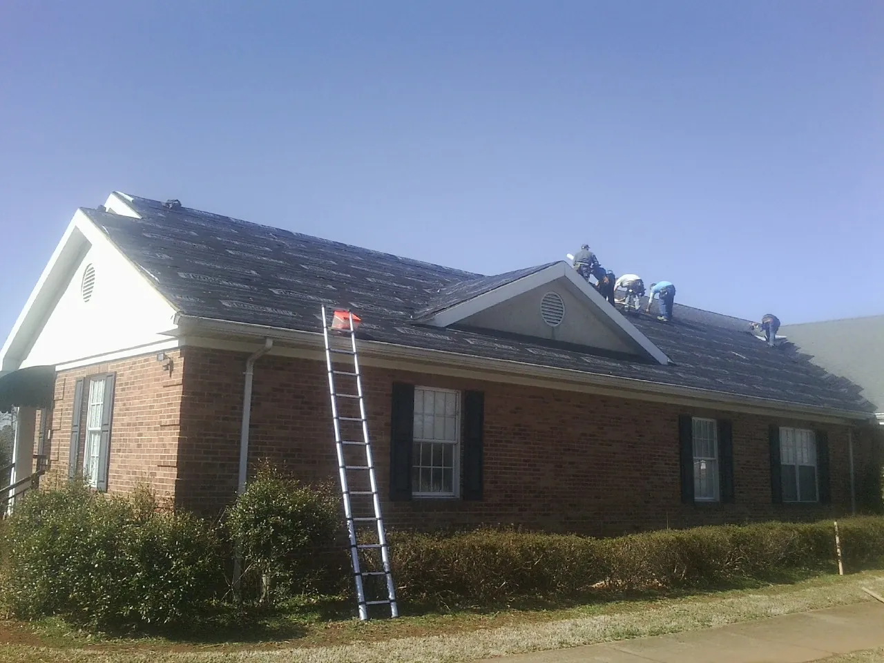 Crew tearing shingles off a brick ranch roof with a ladder set — Emergency Roof Repair work by our crew in Mormon Lake