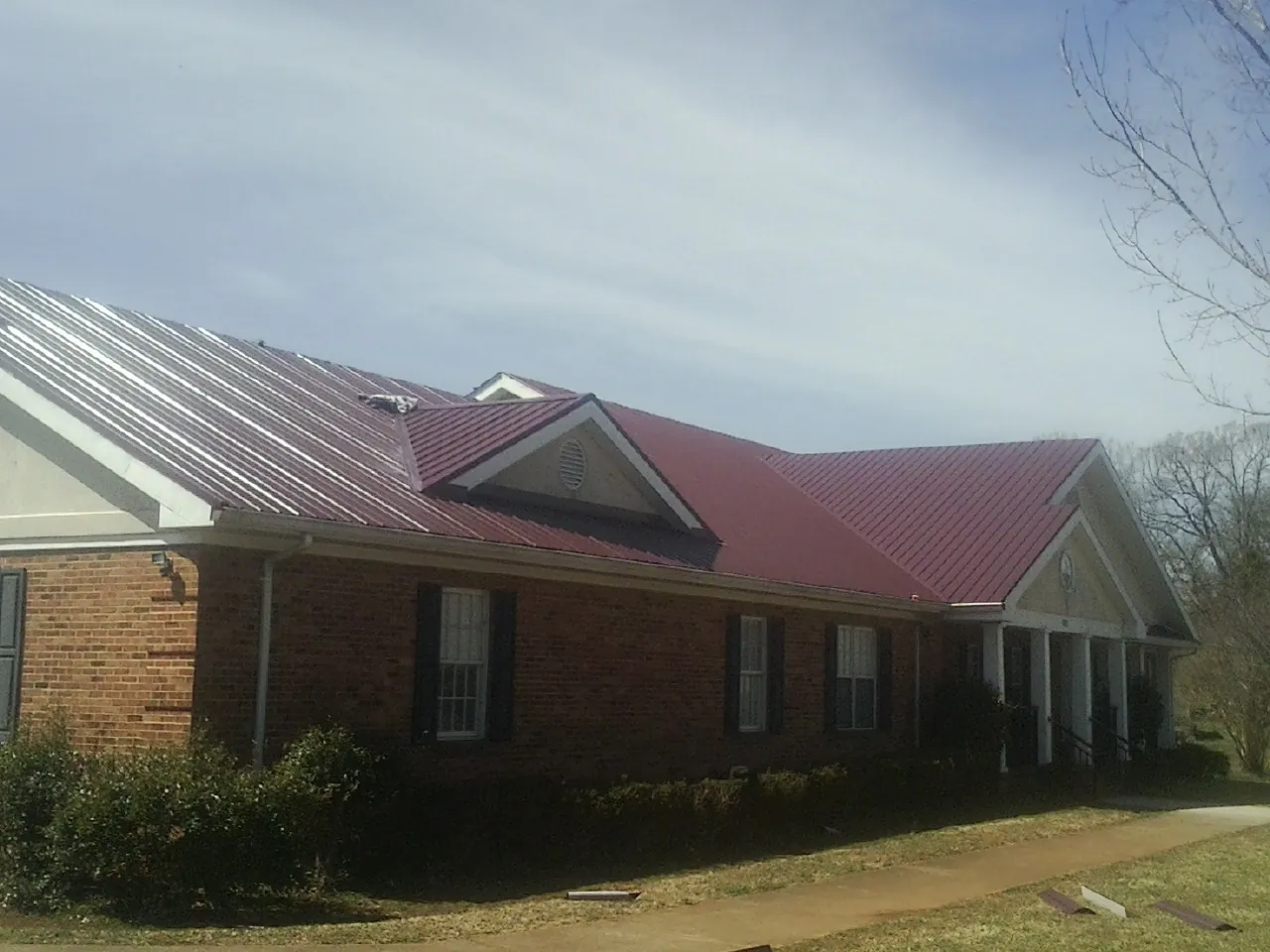 Red metal roof with gabled entries on a long brick building, from a Hail Damage Roof Repair job in Mormon Lake