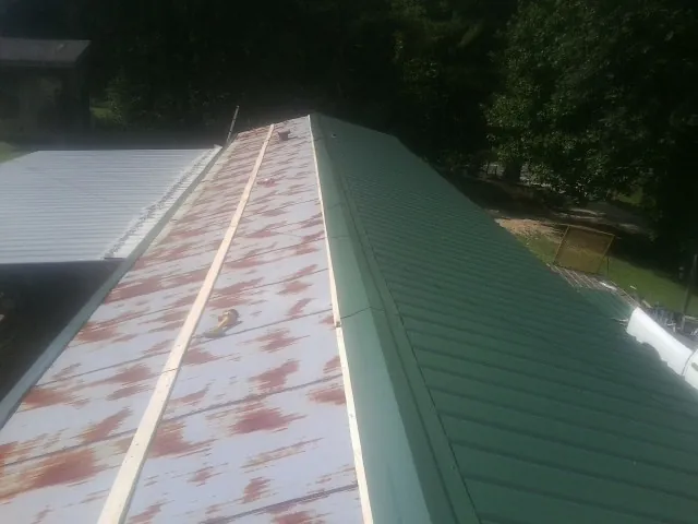 Old rusted panels beside newly installed green metal roofing — Wind Damage Roof Repair by Roofing Brothers in Mormon Lake