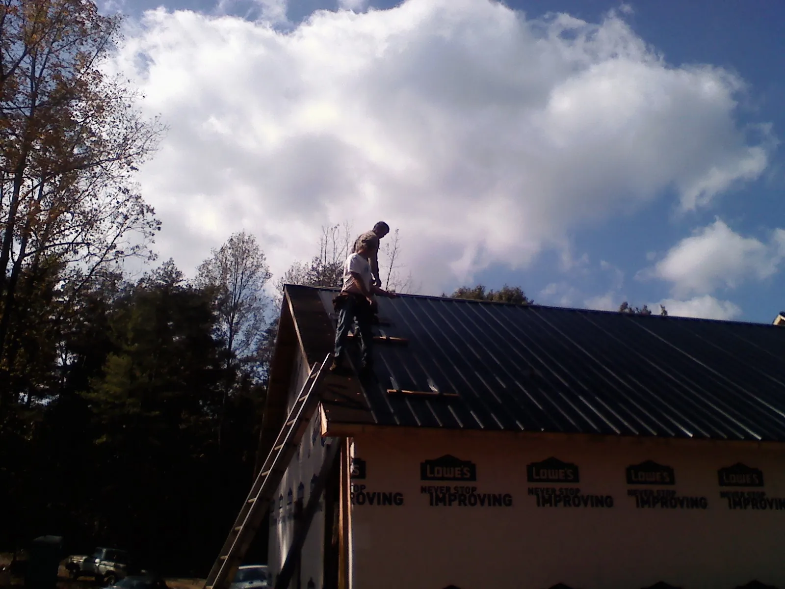 Roofer fastening dark metal panels high against a cloudy sky, from a Roof Inspection job in Mormon Lake