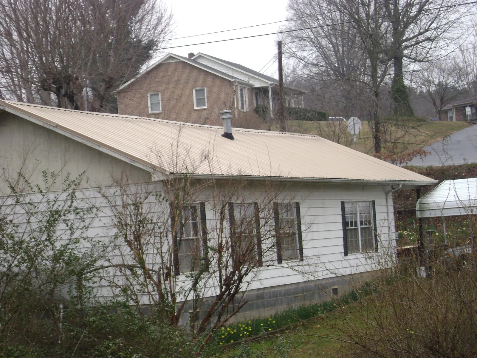 Tan metal roof on a white sided house set into a hillside — Commercial Roofing by Roofing Brothers in Mormon Lake